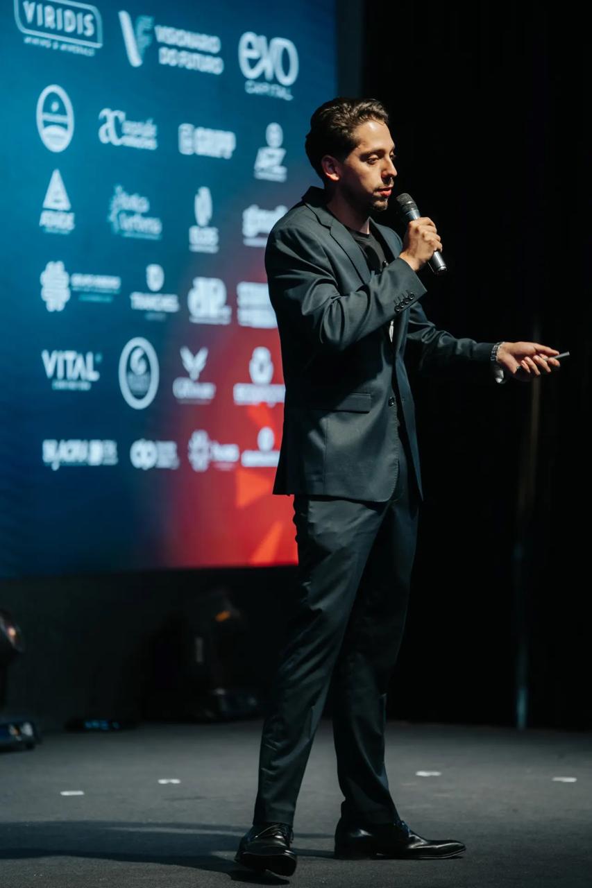 Leonardo Chagas no palco do Empreende Poços 2026, com o telão de patrocinadores ao fundo